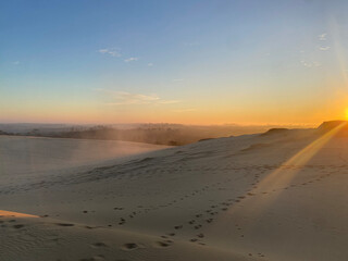 Sunrise over the sand dunes of a desert, with warm golden light casting long shadows and creating beautiful patterns on the rippled sand