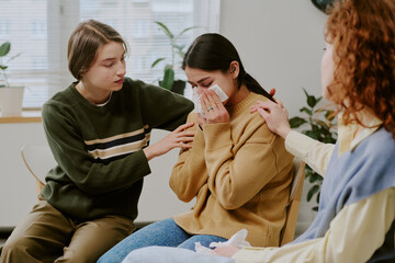 Woman being comforted by two friends in an intimate support group setting in daylight. Emotional moment shared between friends showing empathy and concern