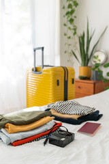 Packing things for the trip. Yellow suitcase and stacks of clothes on the bed in a bedroom