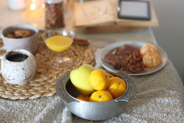 Books, e-reader, tea, orange juice, fruit, snacks, yarn, blanket and lit candles on the table. Autumn or winter hygge at home. Selective focus.