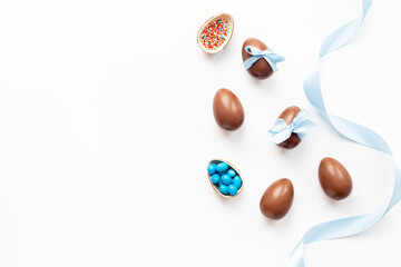 Top view of lots of chocolate Easter eggs with blue ribbon on a white background