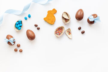 Top view of lots of chocolate Easter eggs with blue ribbon on a white background