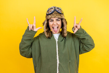 Young beautiful aviator woman wearing vintage pilot helmet with glasses and jacket over yellow...
