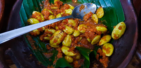 A plate of vibrant regional cuisine showcasing petai stink beans and flavorful red chili sauce,...