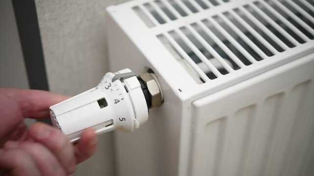 A man adjusts the temperature on a heating radiator in an apartment.