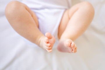 legs of a small child or baby in close-up on a white cotton bed at home