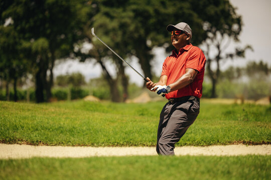 Male golfer executing a bunker escape swing, intensely focused on his shot during a competition