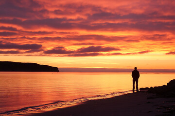 Fototapeta premium Silhouette of a man standing alone on a beach at sunset, gazing at the horizon over calm water, symbolizing solitude, reflection, mindfulness, peace, and the beauty of nature