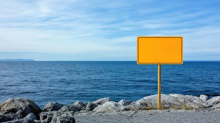 A blank yellow road hazard sign standing near a rocky cliff edge, offering plenty of copy space with a vast sky and ocean view behind.