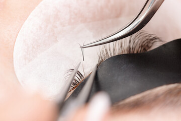 Macro photo eyelash extension procedure on female eye with tweezers