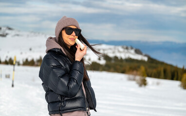 Young Woman applying sunscreen stick in the winter mountain .Spf stick 