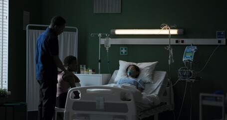 African parents sit near exhausted young sick daughter in hospital ward.