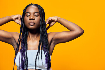 Young Black woman with braids relaxing against a vibrant yellow background, expressing tranquility...