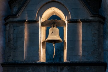 Obraz premium Sunlit church bell in an arched stone belfry.