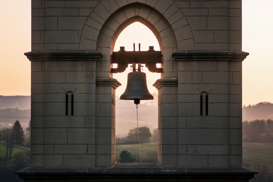 Historic bell tower at sunrise with scenic landscape.