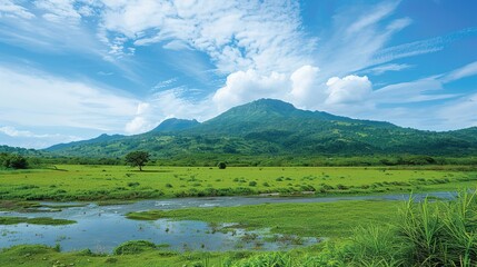 A beautiful green field with a majestic mountain, a clear river and a vast sky in the background. The idyllic and serene natural scenery creates a peaceful and charming atmosphere.