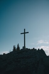 Silhouette of a cross on a rocky hill at dusk.