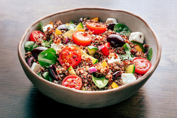 Quinoa salad, healthy Mediterranean lunch with fresh organic vegetables, cheese, and olives, on a dark rustic wooden background