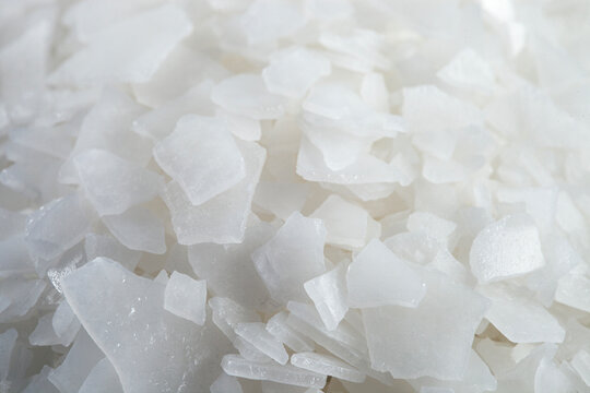 Magnesium chloride flakes -sea salt - close up. Salt flakes and wooden scoop on black background