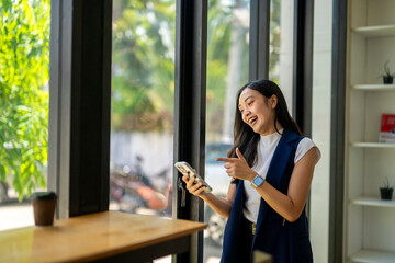 Fototapeta premium A woman is standing in front of a window with a cell phone in her hand