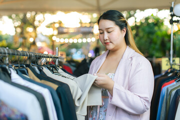 Overweight young woman shopping and thinking about new clothes in street market. Happy plus size...