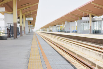 Fototapeta premium a train station platform with a walkway paved with gray tiles. There are yellow and orange parallel strips running along the walkway.