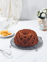 A freshly baked bundt cake rests on a cooling rack beside sliced mango and elegant flowers, creating a delightful pastry display