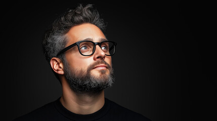 Fototapeta premium Moody portrait of a man with glasses and a beard, captured in deep shadows, highlighting facial features and expression in a dramatic setting