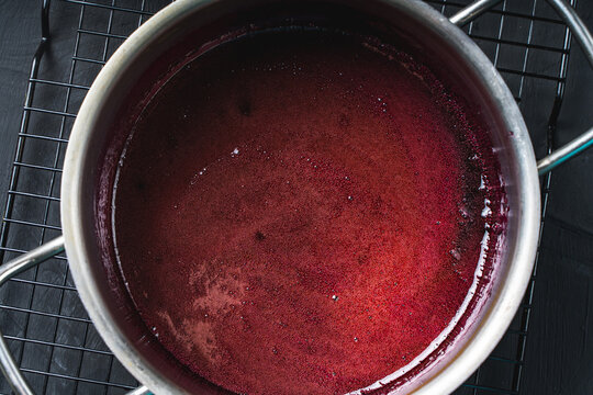 A steel pan with cherry syrup on a black rack. Close-up, Background picture, space for text.
