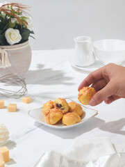 Delicate pastries are arranged on a plate while a hand reaches for one against a minimalist backdrop with floral decor