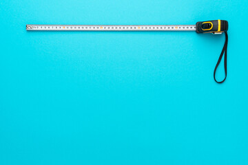 Top view minimalist photo of tape measure on turquoise blue background with copy space. Flat lay image of construction measuring tape.