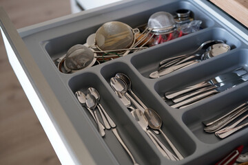 An open drawer with a fitted sideboard. We can see spoons, knives, forks and other utensils.