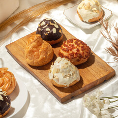 Delicious pastries topped with chocolate, cream, and nuts are elegantly arranged on a wooden board among delicate decor