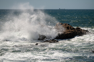 Waves crashing against rocky coast under bright sunlight by the open sea