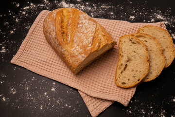 Half a loaf of bread lies on a towel and three slices of the same bread are cut next to it.
