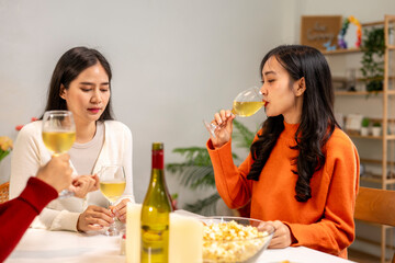 Three women are sitting at a table, drinking wine and eating popcorn