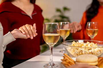 Three women are holding hands and drinking wine at a table
