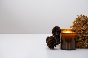 A burning amber glass candle in a cozy setting with dried hydrangeas and mini chrysanthemums. 