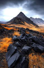 Obraz premium This stunning image captures an otherworldly volcanic landscape, with dramatic peaks and contrasting golden grass, under a moody sky, showcasing nature's raw beauty and power.