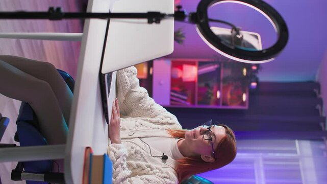 modern professions, female influencer broadcasting live on social media while sitting at a table with a laptop in a modern room, vertical format