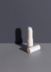 Opened white blank lip balm stick with a lid over a grey with hard shadow top view, mockup
