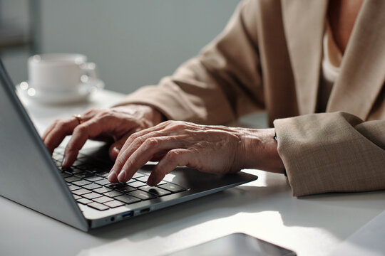 Hands of mature modern businesswoman touching keys of laptop keypad while networking or entering data
