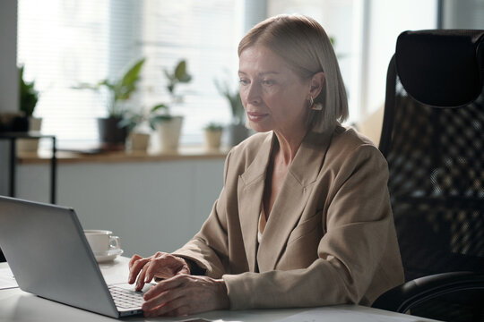 Serious female owner of business company looking at laptop screen while analyzing financial situation on market