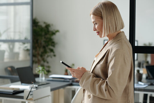 Profile of serious mature office manager texting in mobile phone or watching online video in office