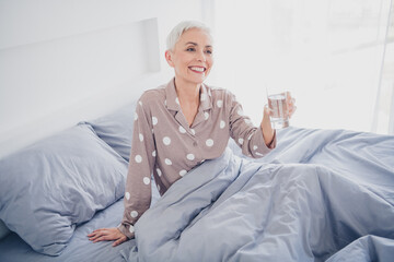 Elderly woman in polka dot sleepwear enjoys morning relaxation in cozy bedroom