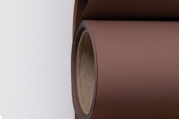 A detailed view of a single roll of dark brown paper against a white background, showcasing its cardboard core. The crisp focus highlights the texture and material