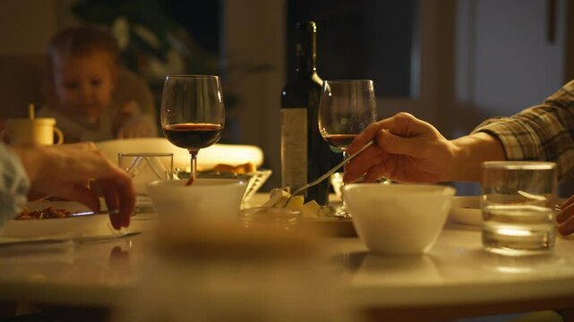 Romantic family dinner. Young married couple sitting at table in evening eating Italian pasta spaghetti drinking wine. Married couple with child having dinner at home in evening