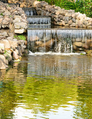 A small cascade of water framed by stone is a decoration of the city park