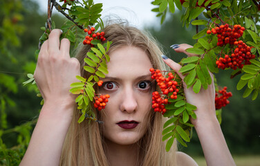 Young woman with striking features gathers red berries in a lush green environment during daytime