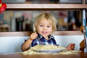 Little baby boy, toddler child, eating spaghetti for lunch and making feeding teddy bear friend